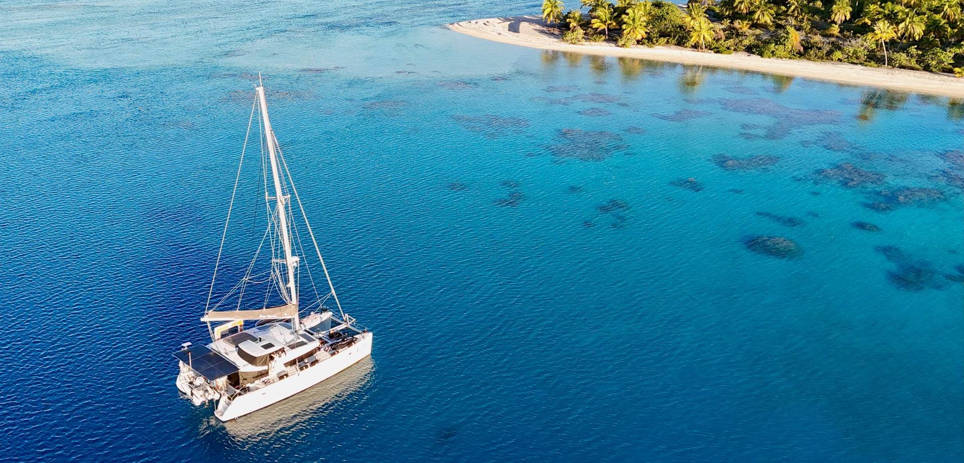 Aerial view of Some Tuesday, a Lagoon 450S catamaran, anchored in clear turquoise water off a palm-fringed island