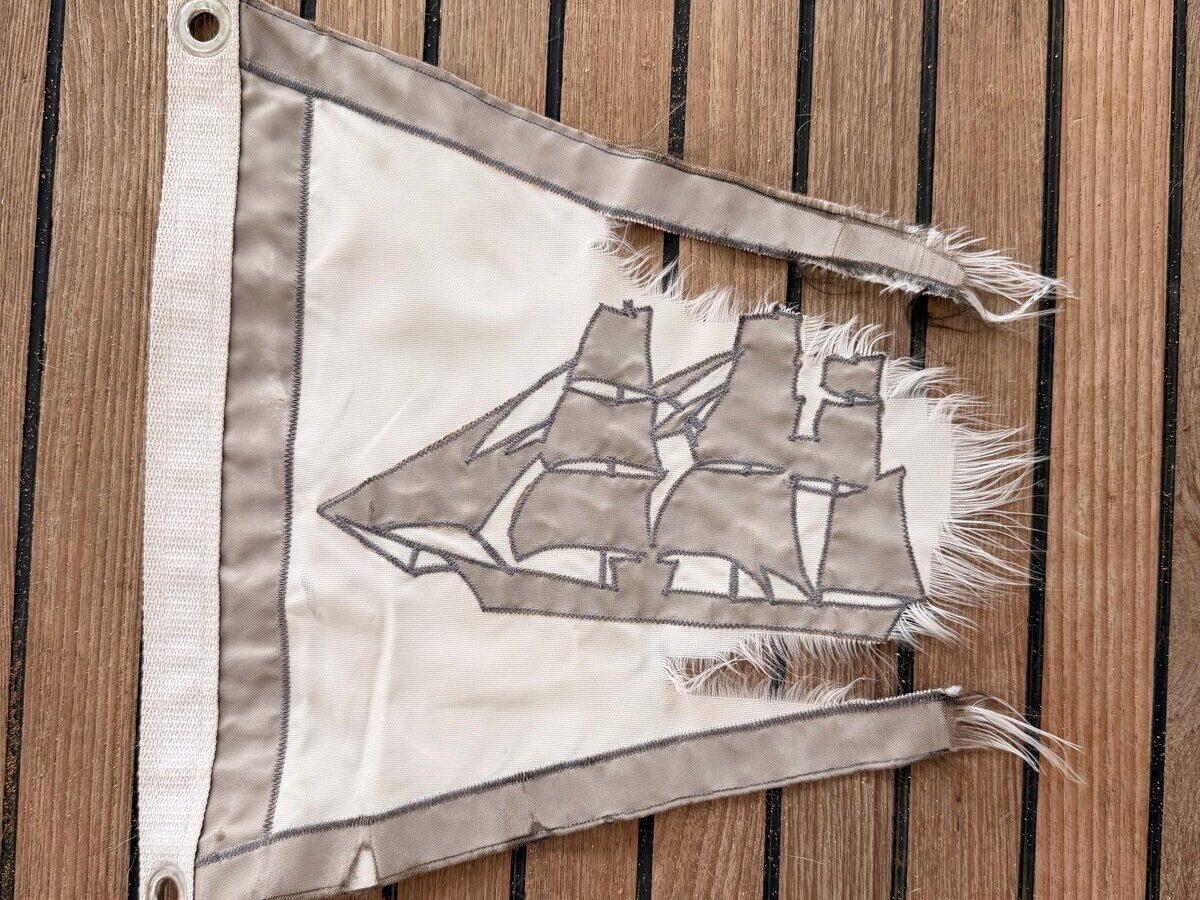 Our tattered Little Ships Fleet Yacht Club burgee laid out on Some Tuesday&rsquo;s teak deck, its fly end frayed to threads