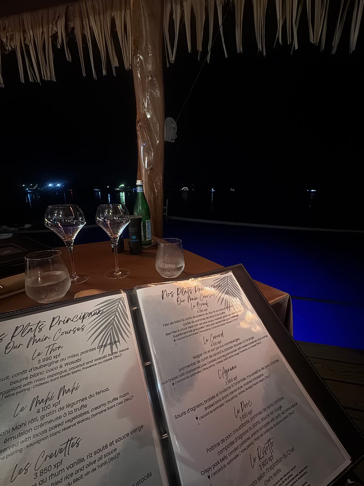 A set dinner table on a deck over the water at night, with candles and string lights, at the Bora Bora Yacht Club
