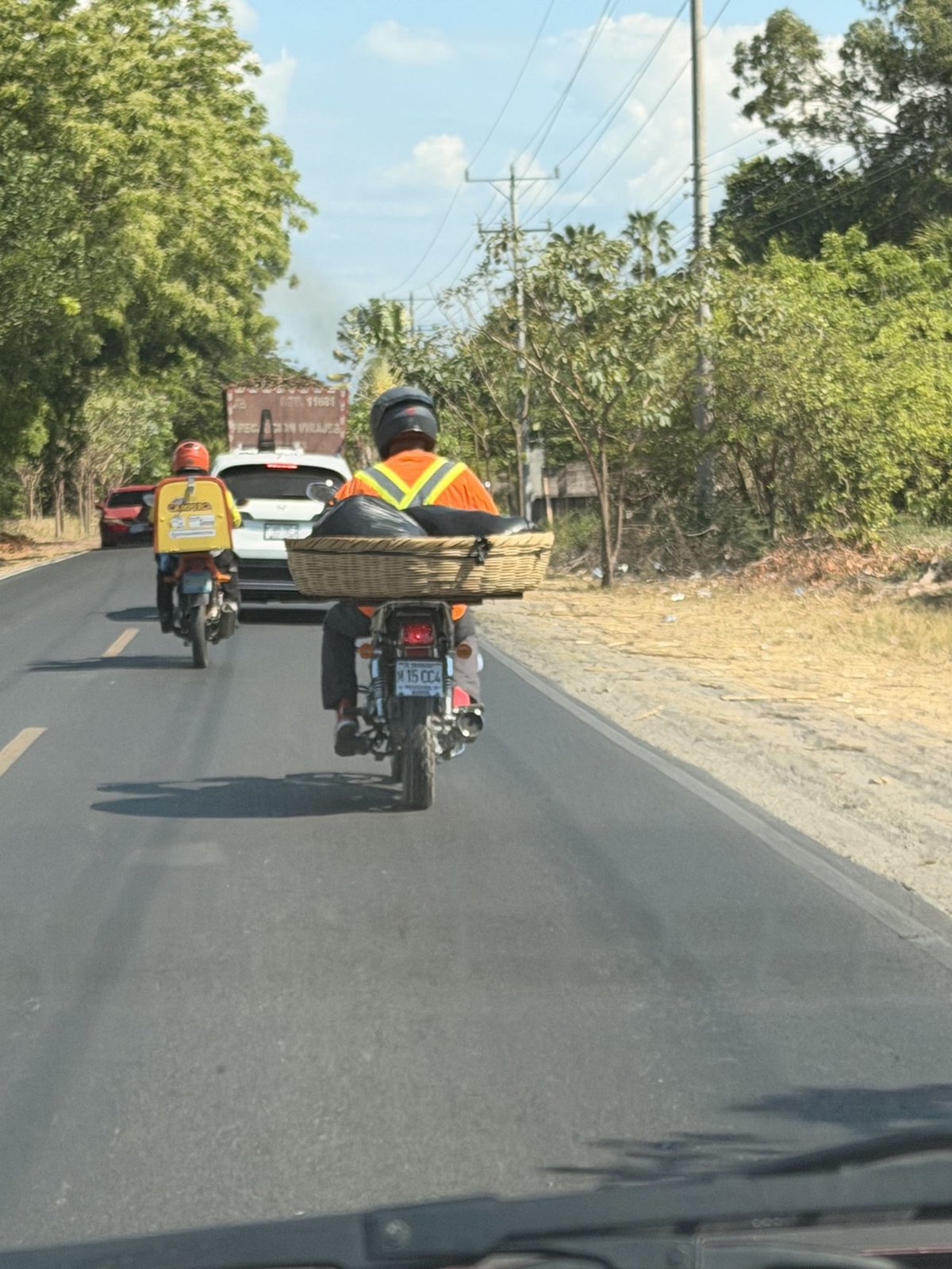 A man on a motorcycle with a huge basket strapped on the back, on a road