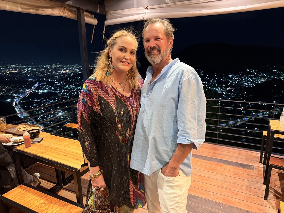 Meghan and Steve standing in a restaurant, with the lights of San Salvador spread out below them