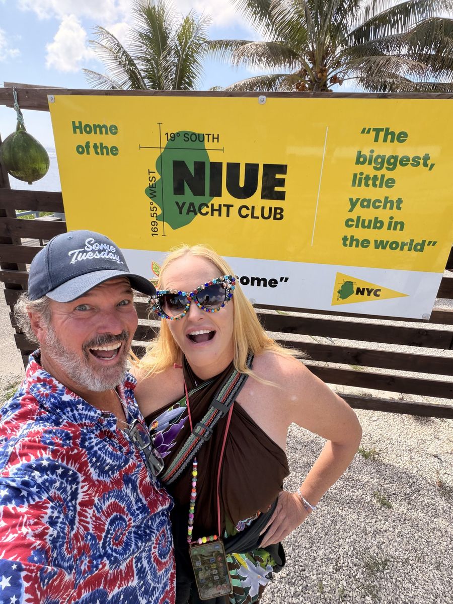 Captain Steve and First Mate Meg standing in front of the yellow Niue Yacht Club sign