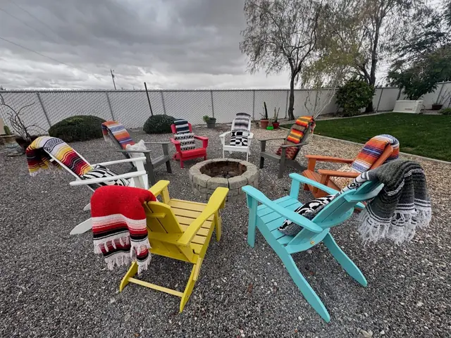 Circle of colourful Adirondack chairs around the stone fire pit