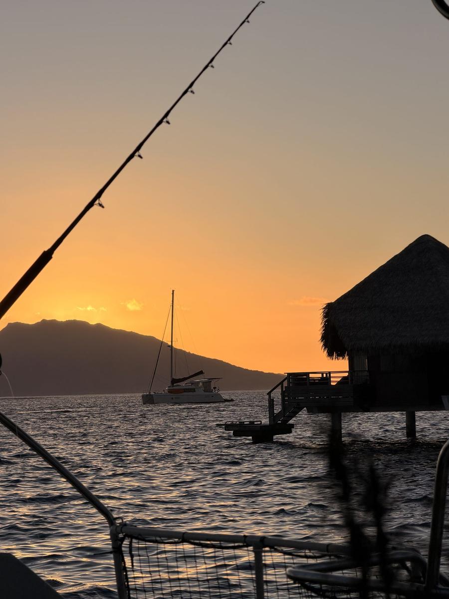 Sunset over a Tahiti anchorage, with a catamaran at anchor and mountains in silhouette