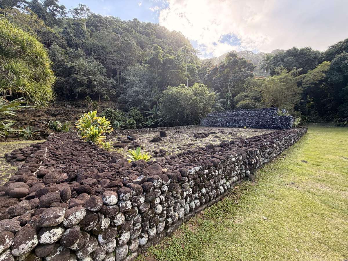 A marae on Tahiti, a stone platform in a clearing, with steep green mountains behind it